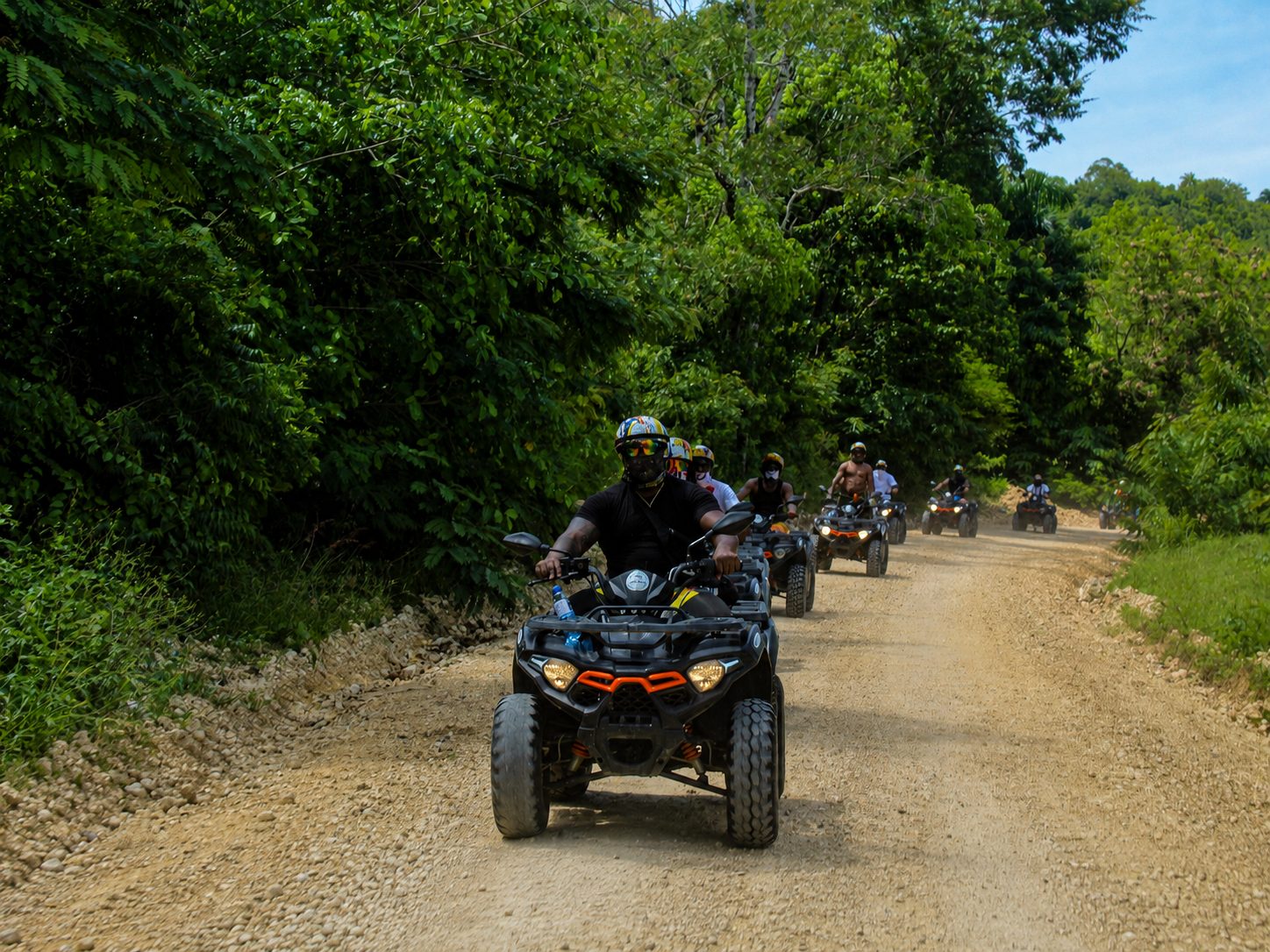 Line of ATV riders on a gravel road through lush green forest on a BlueCasas ATV tour