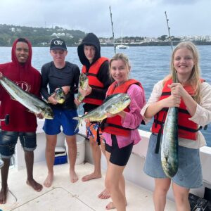 Group of guests holding mahi-mahi (dorado) caught on a BlueCasas fishing tour, with the Dominican north-coast shoreline behind