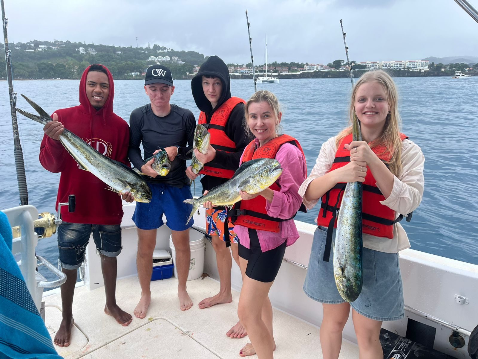Group of guests holding mahi-mahi (dorado) caught on a BlueCasas fishing tour, with the Dominican north-coast shoreline behind